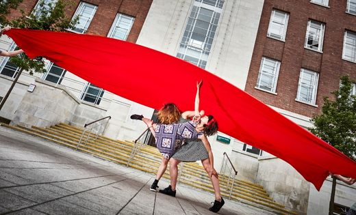 Students dancing on campus, with a backdrop of a red piece of cloth.
