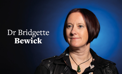 Dr Bridgette Bewick, in black, standing in front of a blue colour splash.