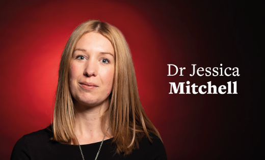Dr Jessica Mitchell, in black, stands in front of a red colour splash.