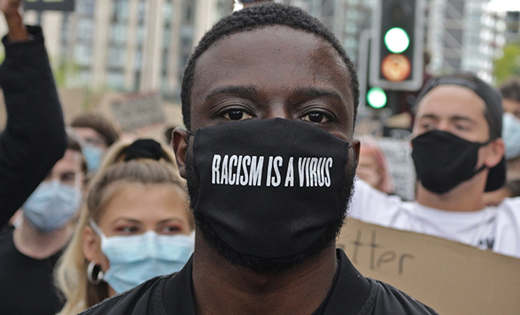 A portrait of a man wearing a mask that says: 'Racism is a virus'.