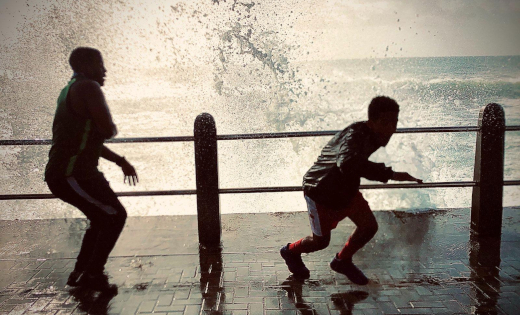 Two people ducking out of the way of a splashing wave at the sea front.