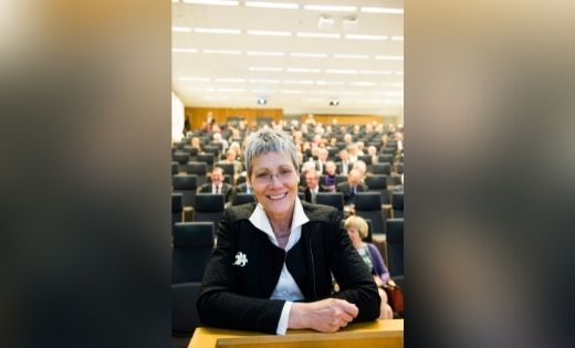 A portrait image of Professor Trudie Roberts sat at the front of a lecture theatre.