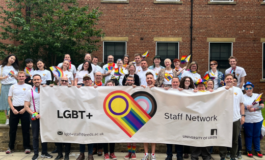 Group picture of the LGBT Staff Network holding the Network Banner outside of the EC Stoner Building before Leeds Pride. The banner is cream with a progress flag love heart symbol and reads "LGBT+ Staff Network"