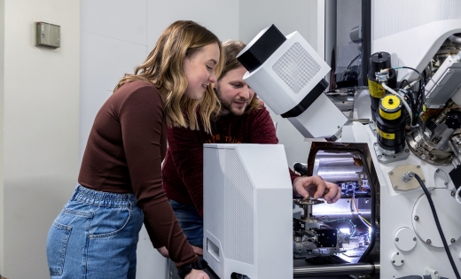 A man and a woman look inside a large technical microscope