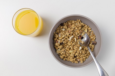 Photo of bowl of cereal with spoon and a glass of orange juice from above.